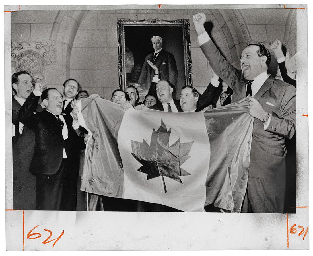 A group of men in suits cheer, holding a Canada flag in front of them