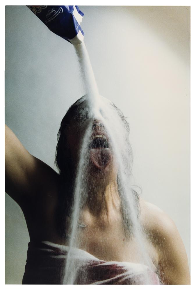 Photo of woman in towel pouring salt from a bag over her head onto her face with an open mouth.