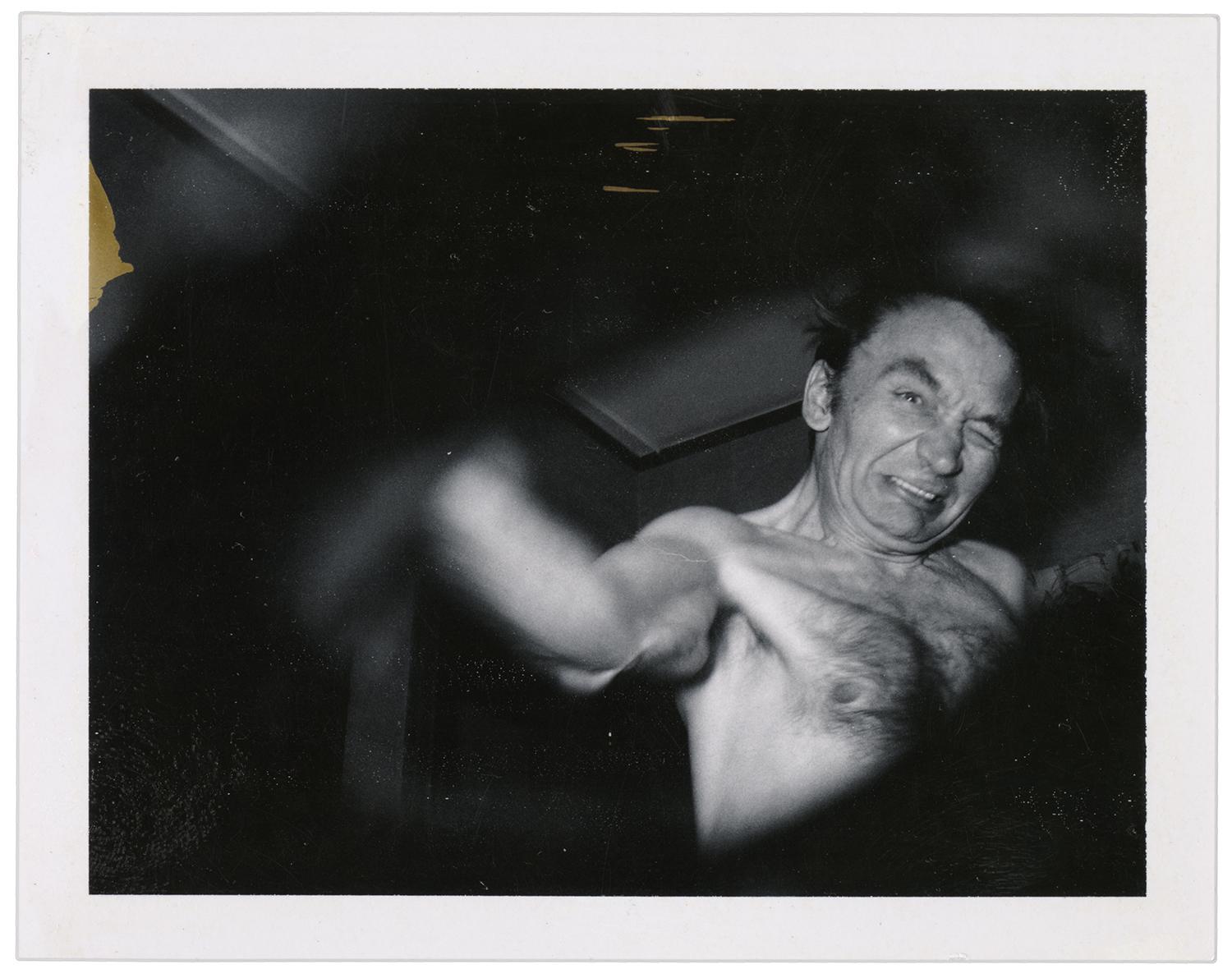 shirtless man, arm outstretched towards lens, strained expression
