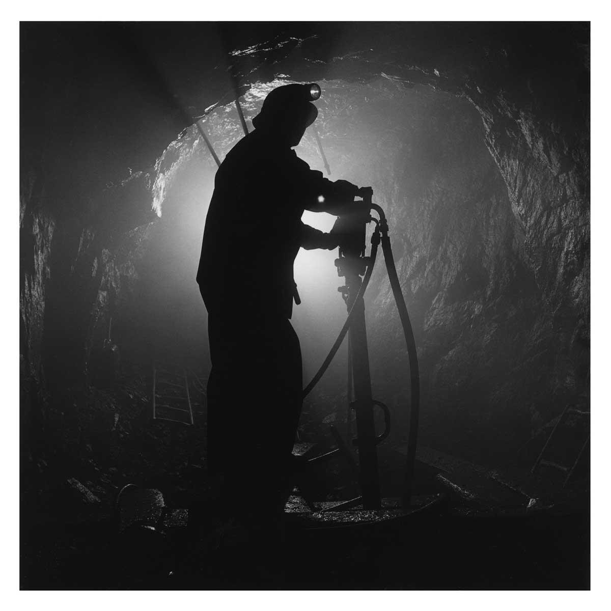 A black and white photo of a backlit minor working underground.