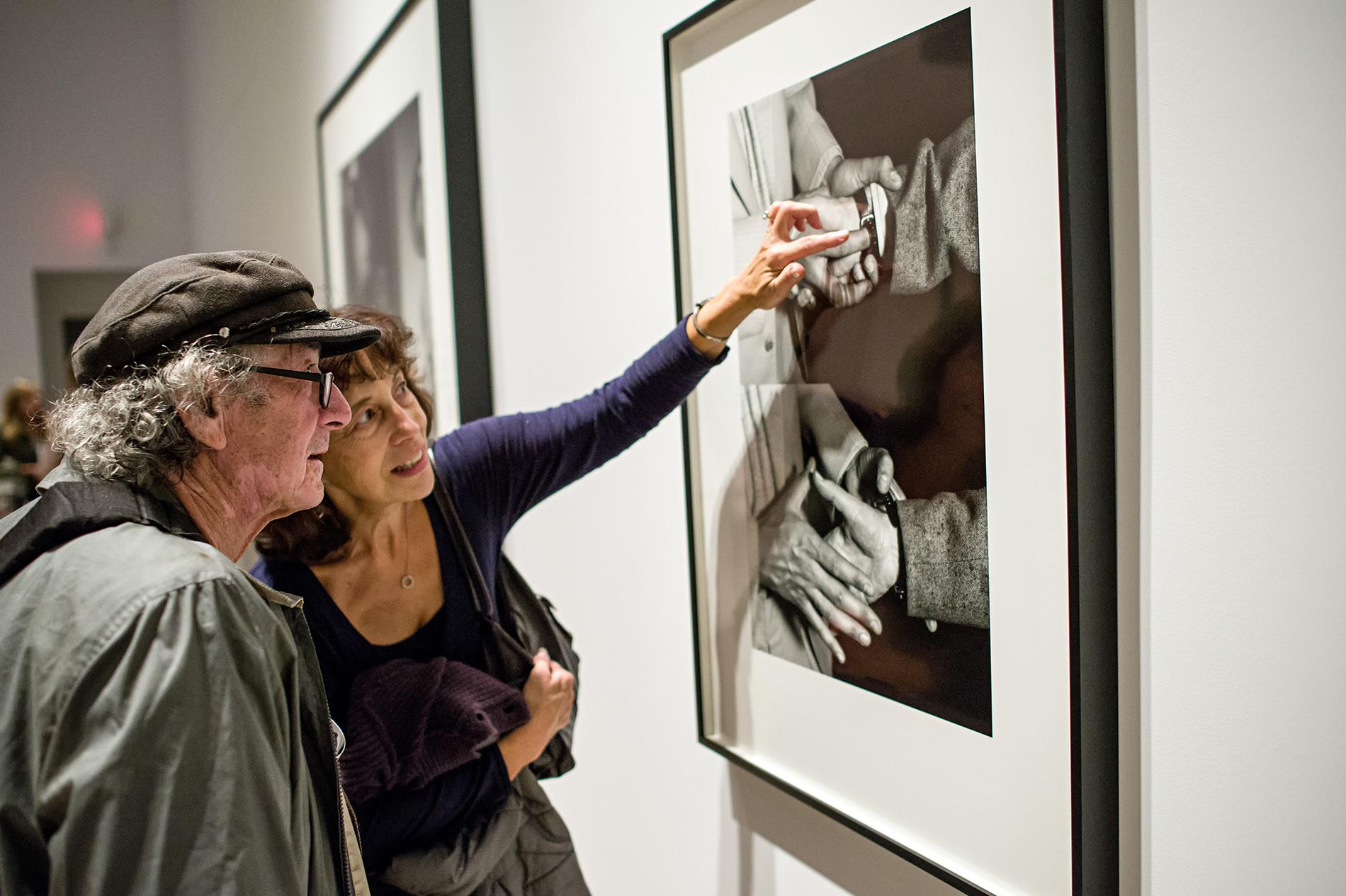 A man and woman looking at a black and white photograph on a wall.