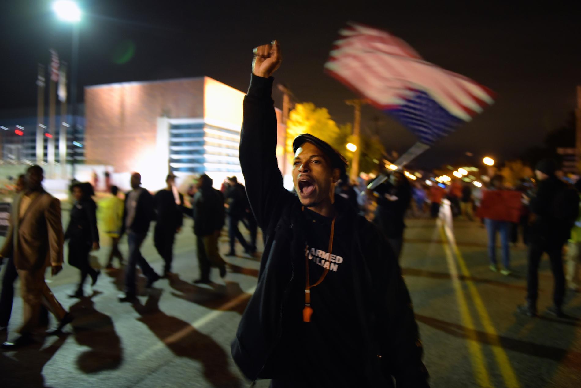 A protestor raising his fist and chanting, an American flag in the background
