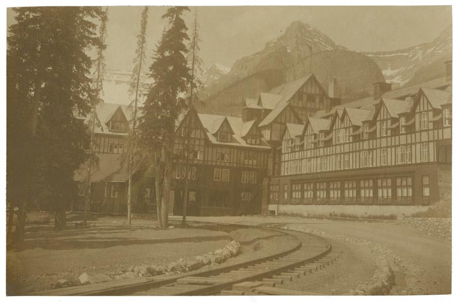 Timber framed buildings behind railroad tracks with mountains behind. Black and white photograph by Minna Keene.
