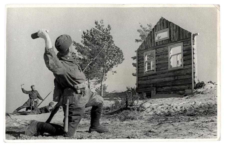 Soldier in training in the act of throwing a projectile towards the facade of a one-wall house front