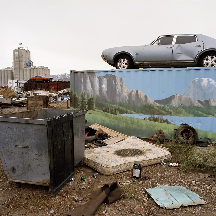 A garbage dump with a dumpster, an old car atop a shipping container, and a stained mattress