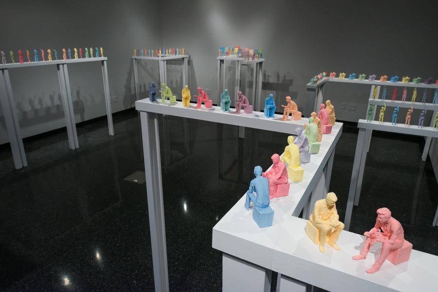 Multiple miniature colourful figurines of men sitting are arranged in a zig zag pattern