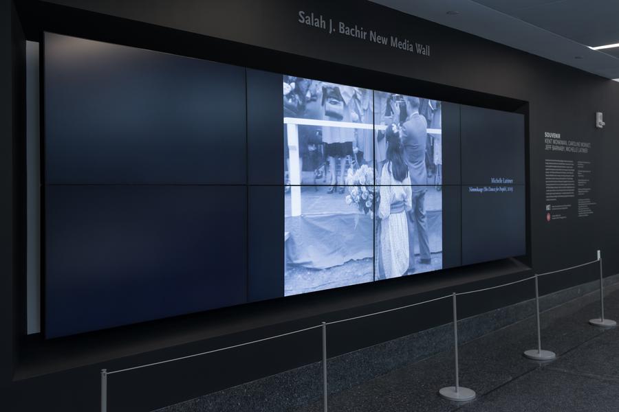 Screen showing a woman holding a bouquet of flowers. Text on the wall behind the screen reads 'Salah J. Bachir New Media Wall'