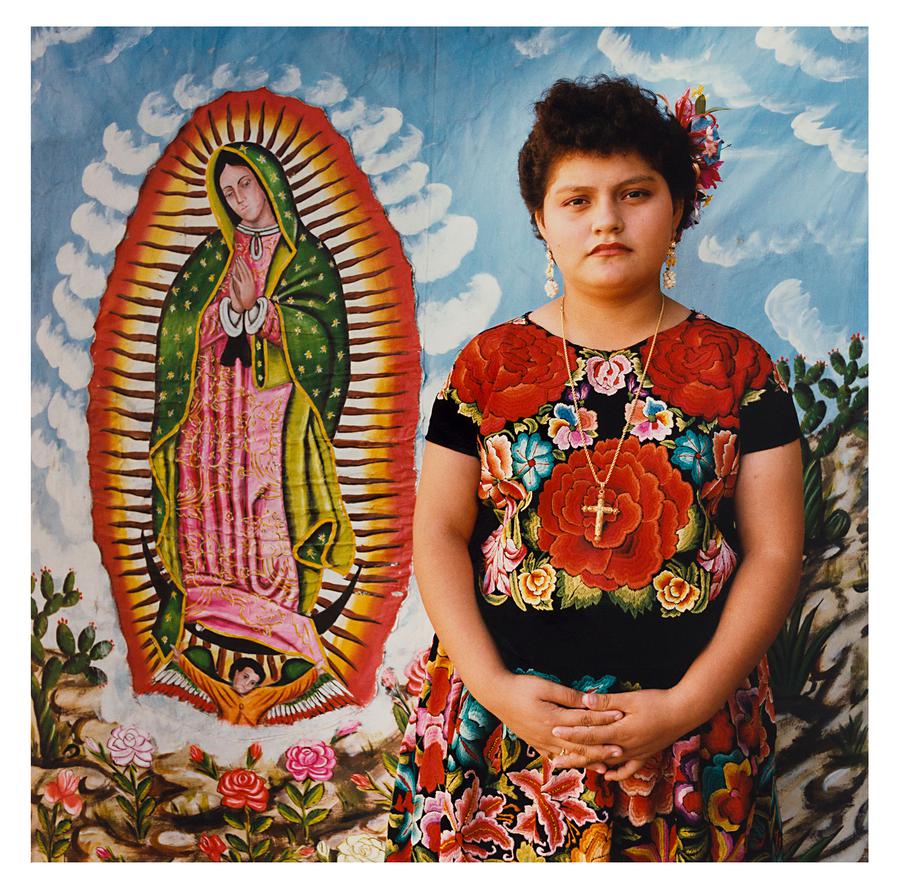 A girl in brightly coloured dress, photographed in front of a colourful background, in Oaxaca, Mexico