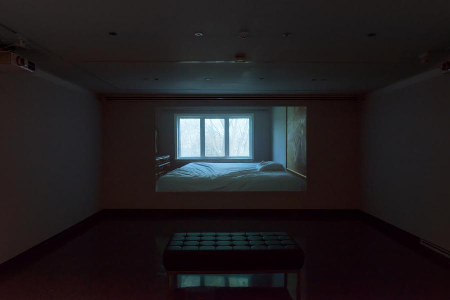 Video still of a bed beside a three-panel window