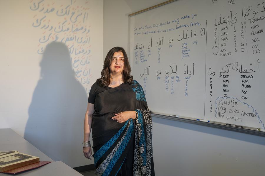 A woman in a classroom standing in front of a white board with writing on it