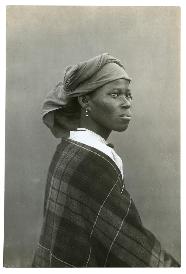 A black and white portrait of a woman seated, in side profile, with a dangling earring, and a headwrap.