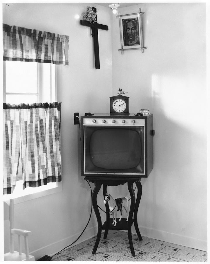 A vintage television on a delicate stand, a crucifix hung above it