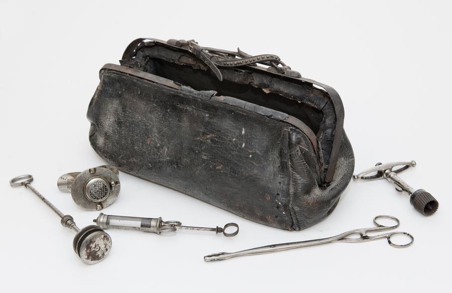 An old black leather bag with veterinary instruments strewn around it