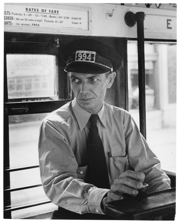 A man drives a streetcar. wearing a black tie and a conductor's hat with the number 994