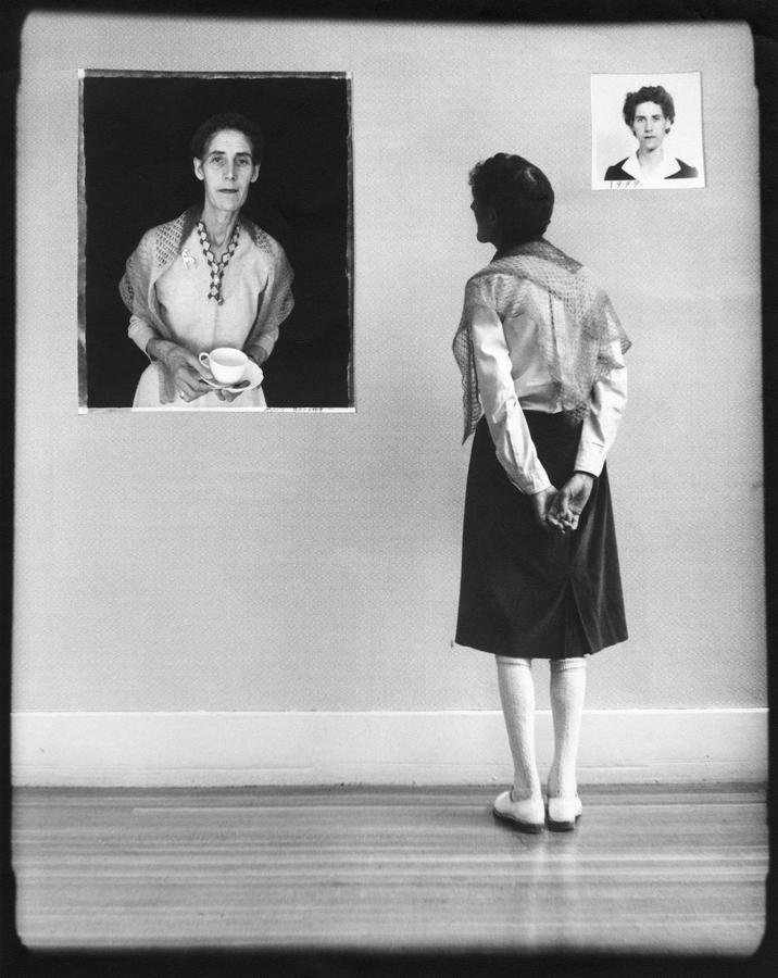 A woman in a black skirt examines a portrait of herself