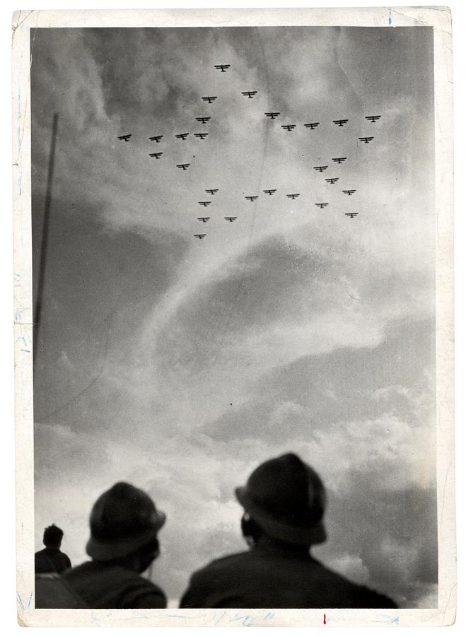Soviet airplanes fly in a star formation, soldiers look up at them from the ground below