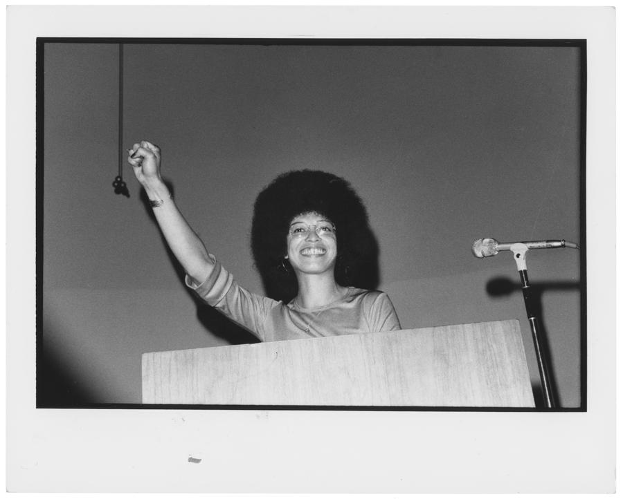 A smiling woman standing at a podium raising her fist in celebration