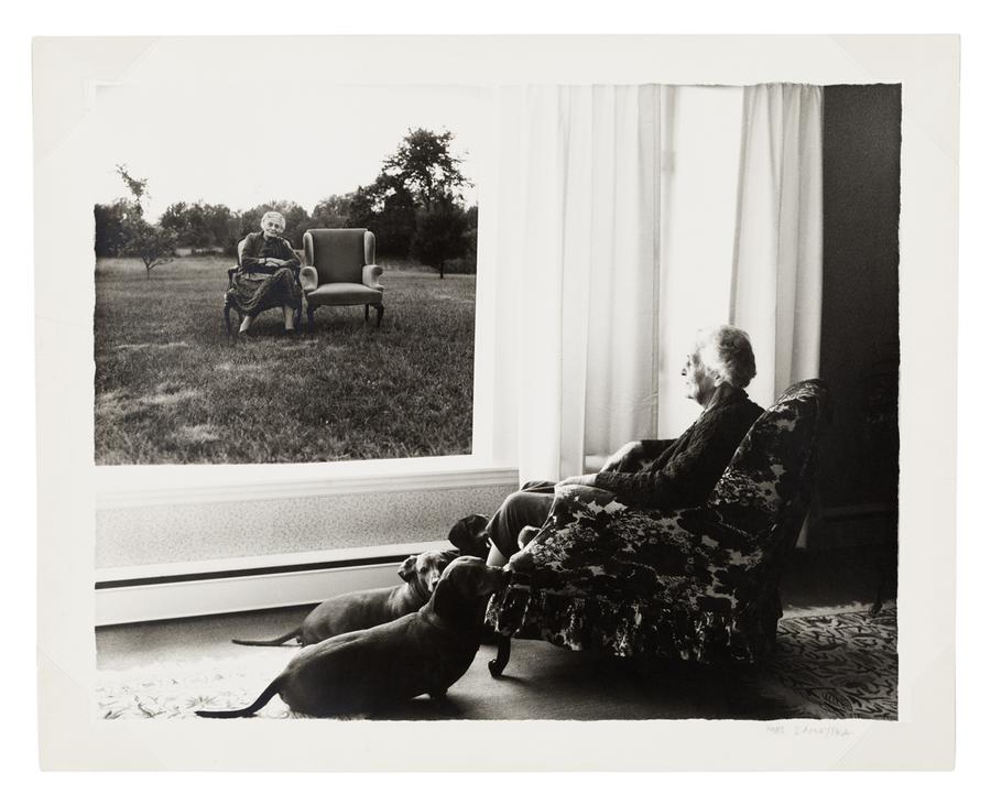 Mrs. Zamoyska sitting in a chair surrounded by her dogs, viewing a picture added in post-production of herself sitting next to an empty chair.
