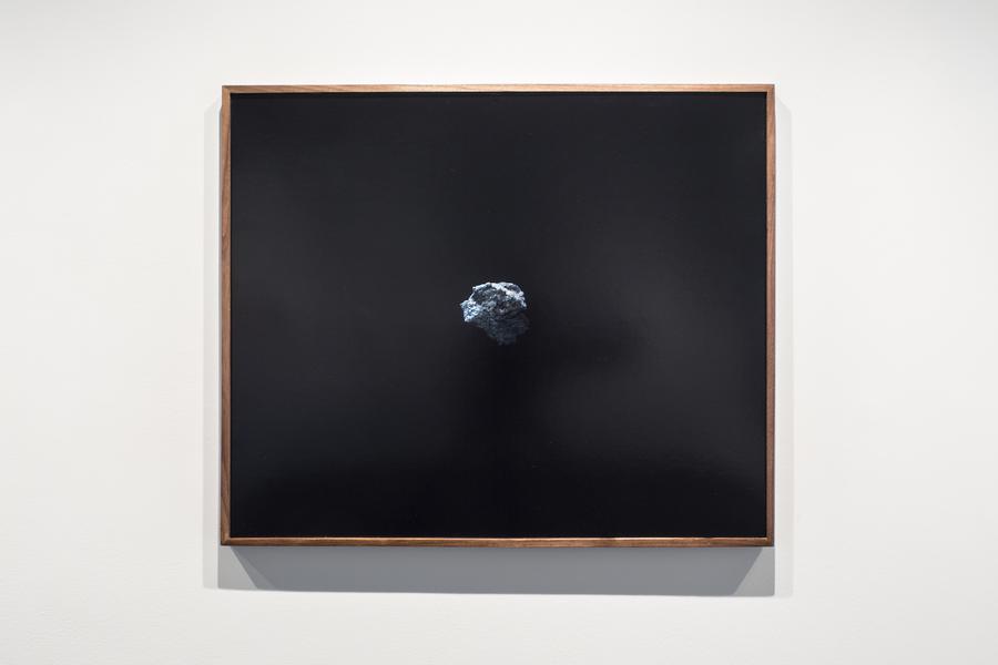 Photograph of a rock on a black background, framed on a white wall