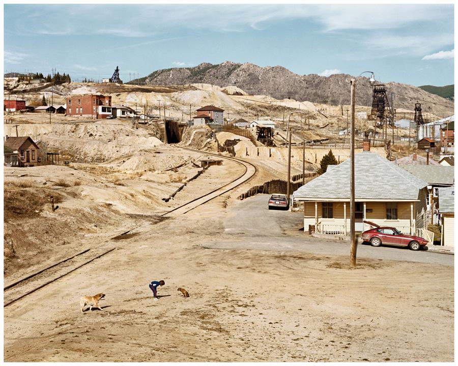 Photograph by Edward Burtynsky. A town located in a desert landscape with a railroad track running through it.