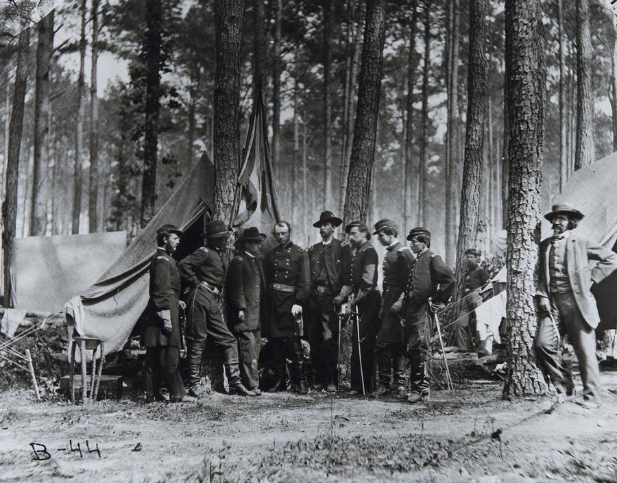 A group of soldiers stand in the forest in front of a tent