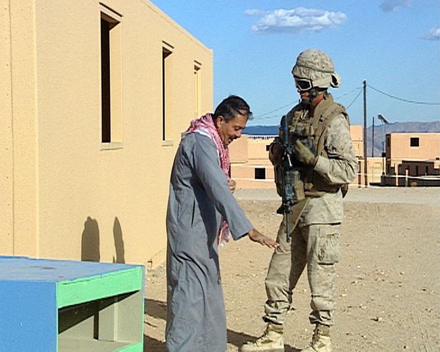 Video still of a man in grey speaking to a soldier holding a gun