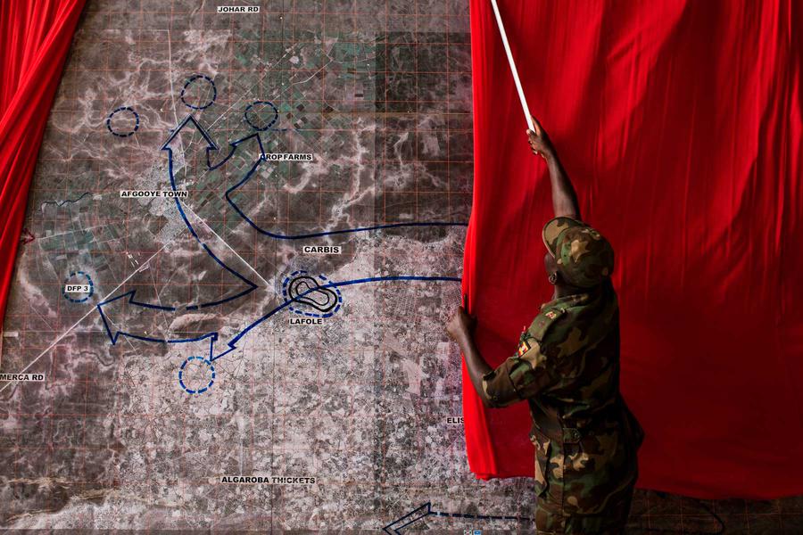 A soldier pulling a red curtain over a map on the wall