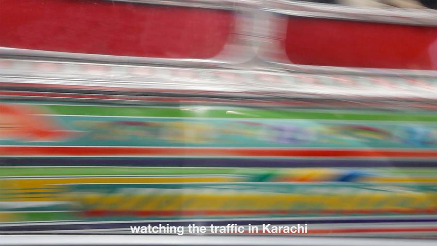 Blurry video still of a bus in motion. Text reads "watching the traffic in Karachi"