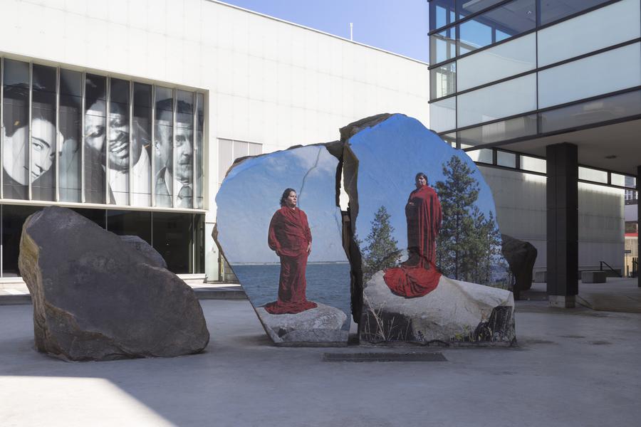 Two images of women in long red cloaks printed onto large rocks at Ryerson's Lake Devo