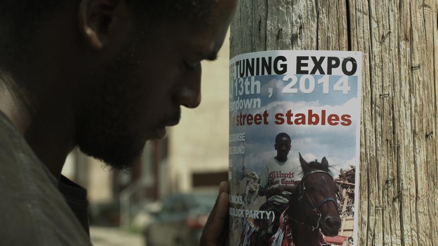 A man puts up a poster for a horse-riding expo on a street pole.