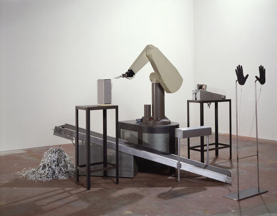 A mechanical arm sits atop a conveyor belt, a pile of paper shreds at the end