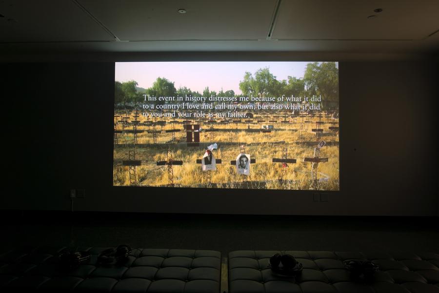 Video still in a dark room. On-screen text reads "This event in history distresses me because of what it did to a country I love and call my own, but also what it did to you and your as my father"