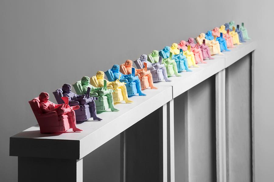Multiple miniature colourful figurines of men sitting and reading the newspaper are posed on a beam