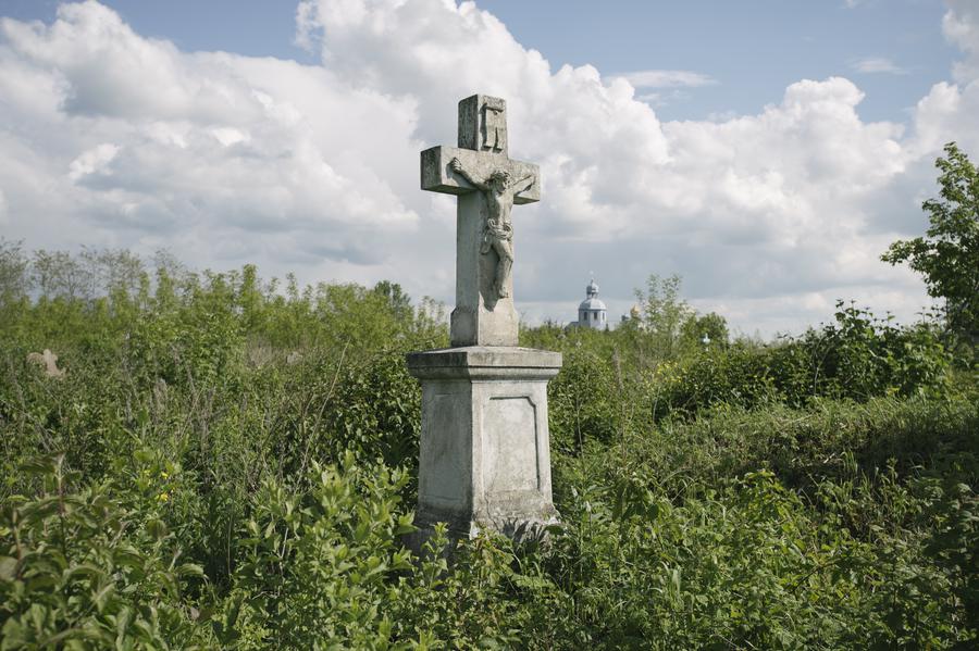 Gravestone with a cross in the middle of an overgrown field