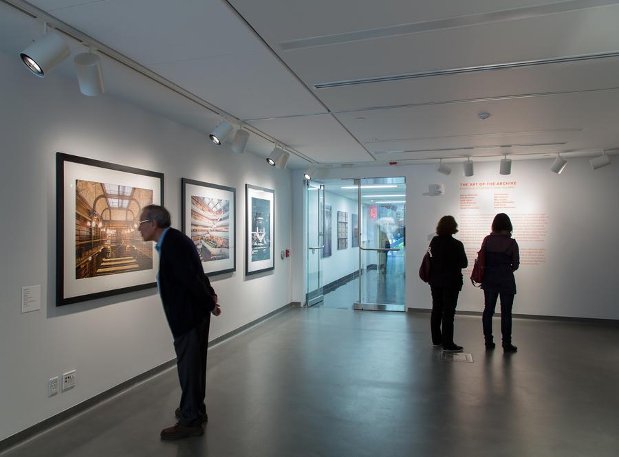 A man, alone, and two women examine photographs in the gallery