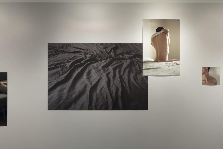 A photograph of grey sheets, and a photograph of a man taking off a white shirt, both on a white wall