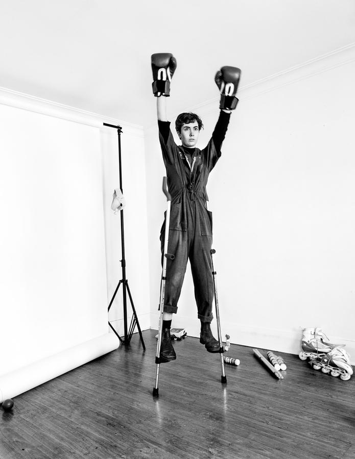 A woman stands on stilts wearing boxing gloves. Haley Wilsdon, Stilt Boxing, at the Ryerson Image Centre.