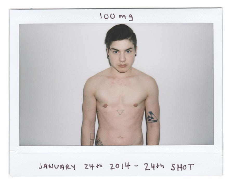 A shirtless man in front of a white wall staring at the camera. The handwritten text reads "100 mg. January 24th 2014. 24th shot."