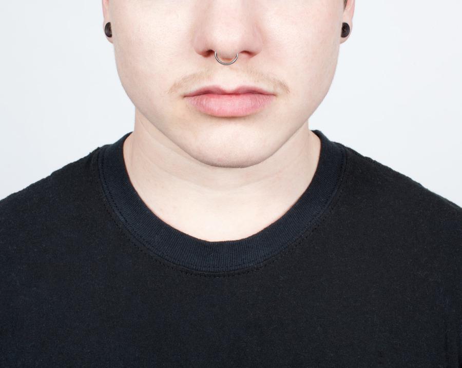 A man in a black tshirt with a moustache, a nose ring, and black earrings