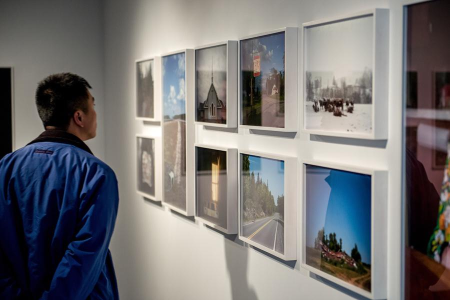 A man in a blue jacket examines a series of framed photographs