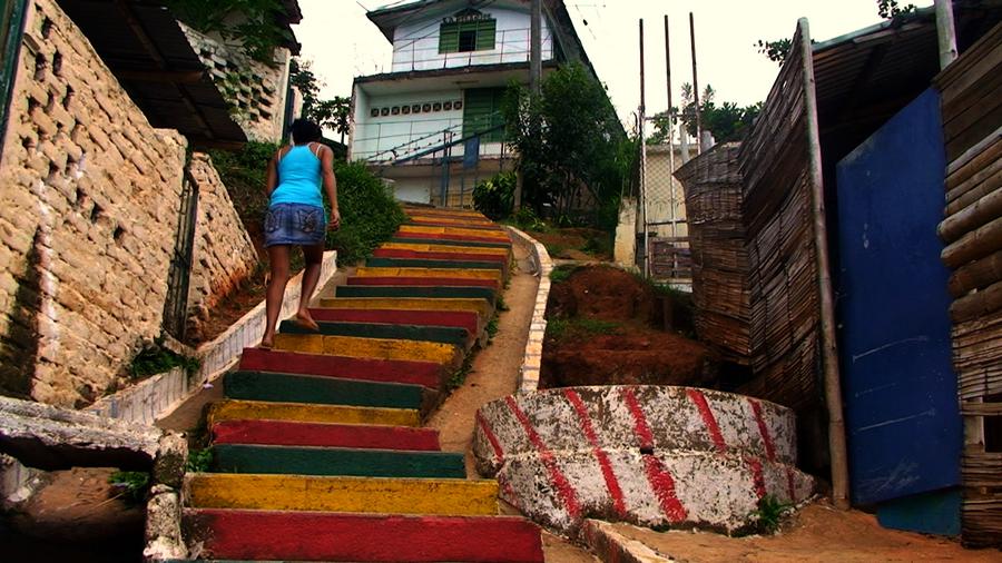 A woman, barefoot in a skirt and tank top, walks up a flight of brightly-coloured stairs