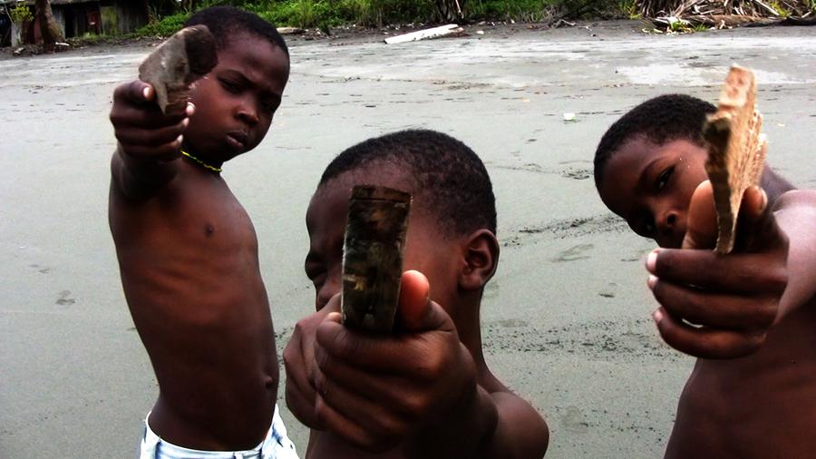 Three young boys hold pieces of wood like guns