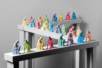 Multiple miniature colourful figurines of men sitting are arranged in a zig zag pattern