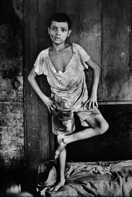 A young, poor boy poses in tattered clothing