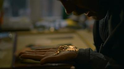 A close up of a man with his palm open, holding a gold substance