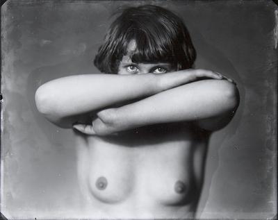 A young women who is topless and covering the lower part of her face with her arms